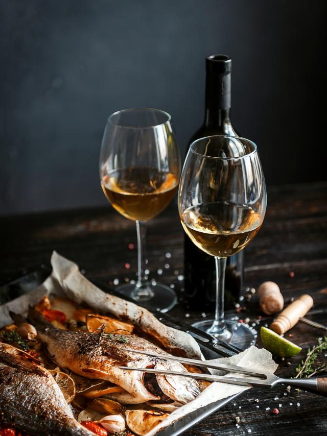 dinner concept for two. two glasses of white wine, baked fish.